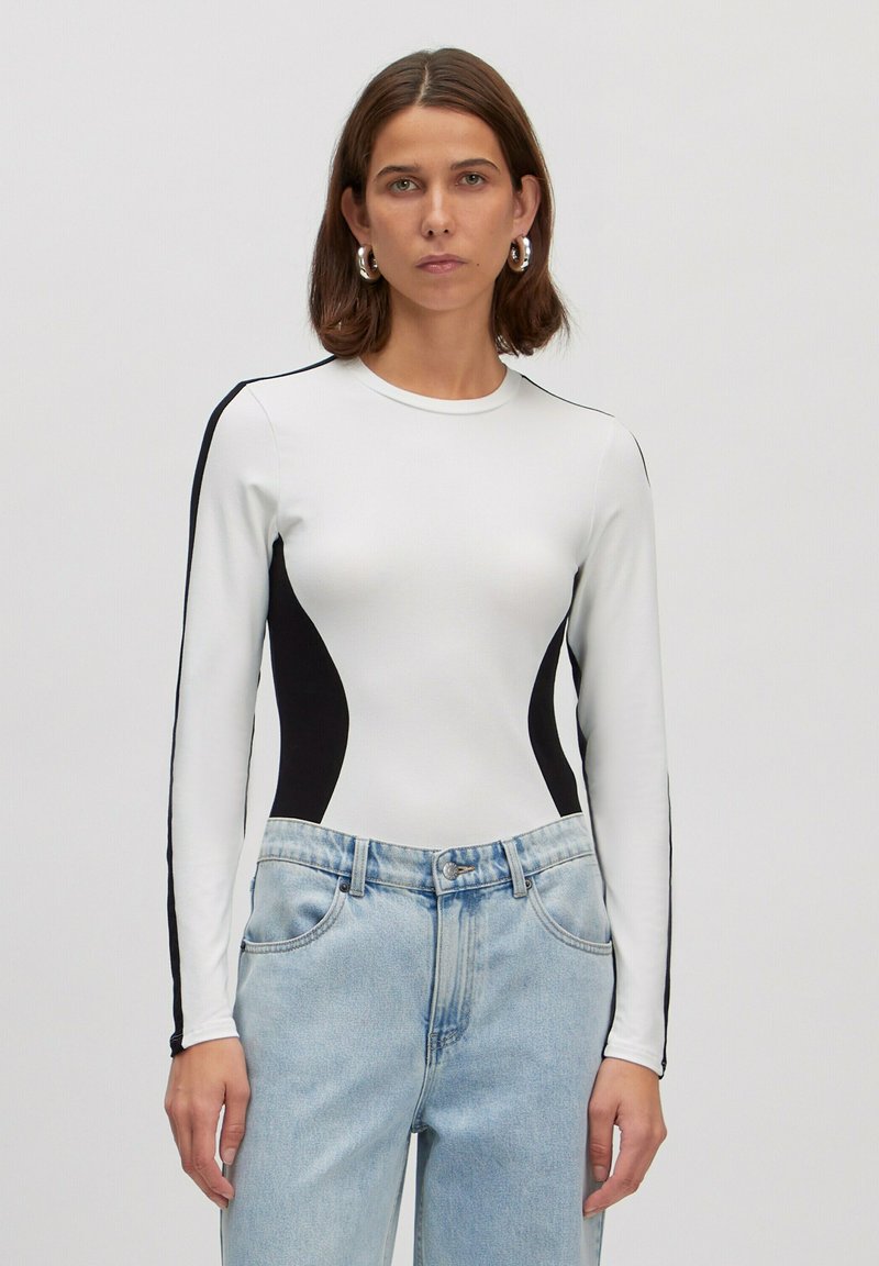 Witte lange mouwen bodysuit met zwarte zijkanten, ronde halslijn en rekbare stof. Gecombineerd met lichtgewassen denim broek.