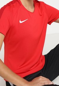 Rood atletisch T-shirt gemaakt van lichtgewicht stof, met een ronde hals, korte mouwen en een wit Nike-logo op de borst.