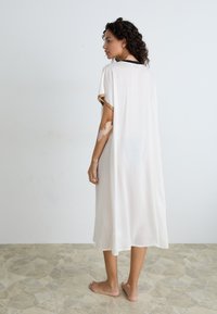 White, lightweight, knee-length dress with short sleeves and gold trim. Soft, flowing fabric with a loose fit. Plain design.