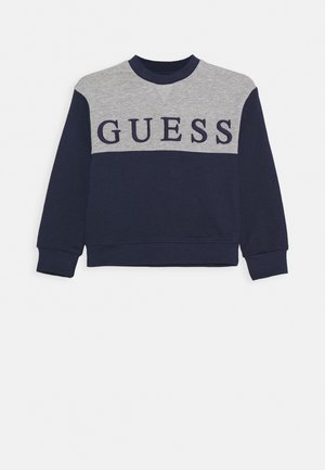 Sweat-shirt à manches longues bleu marine et gris avec "GUESS" en grandes lettres bleu marine sur la poitrine.