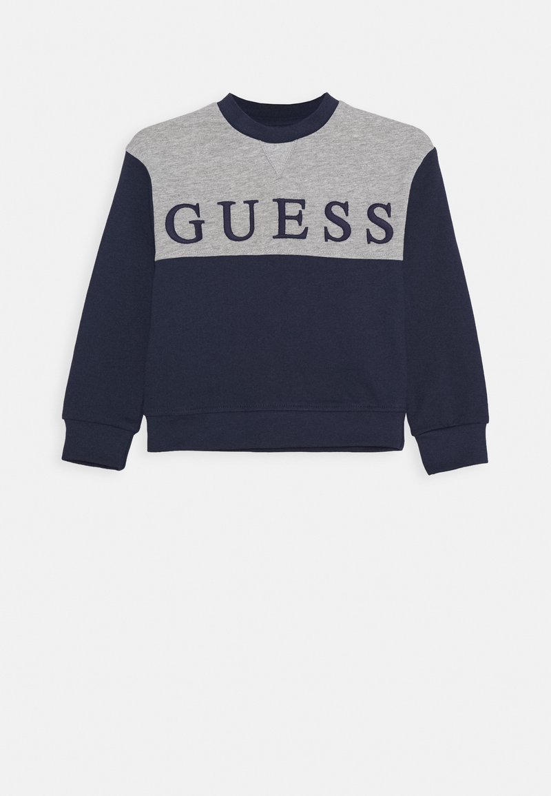 Sweat-shirt à manches longues bleu marine et gris avec "GUESS" en grandes lettres bleu marine sur la poitrine.