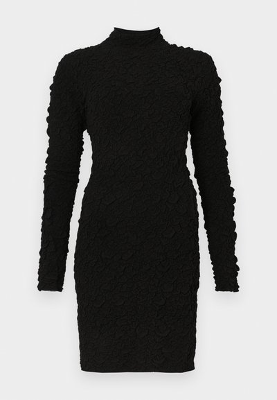 Must tekstuuriga pikkade varrukatega mini kleit kõrge kaelusega ja vormitud siluetiga ühevärvilise tausta ees.