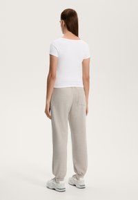 Bílá pevně střižená košile s krátkým rukávem, spárovaná s světle šedými tepláky s elastickými manžetami a zadní kapsou. Obuv: bílé tenisky.