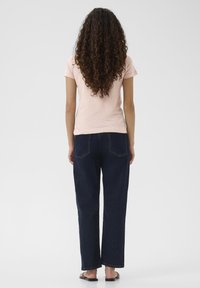 Ein hellrosa eng anliegendes T-Shirt mit kurzen Ärmeln, kombiniert mit einer lässigen, dunkelblauen Jeans im Loose-Fit-Stil mit zwei Gesäßtaschen und geradem Bein.
