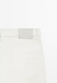 Vue arrière d'un jean en denim blanc montrant les passants de ceinture, une poche arrière, et une étiquette gris clair avec le nom de la marque "Massimo Dutti".