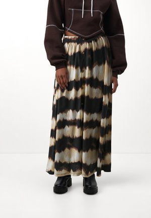 Maxi rok in een tie-dye patroon met zwarte, crème en bruine tinten, met een knoopsluiting aan de voorkant en geplooide textuur. Gecombineerd met een bruine cropped hoodie.