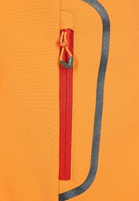 Oranssi urheilutakki, jossa on punainen vetoketjullinen tasku ja teksturoitu kangas. Harmaa korostusviiva juoksee taskun vieressä.
