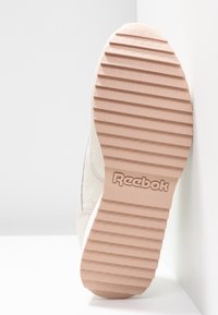 Valkoinen urheilukengän pohja, jossa on teksturoitu vaaleanpunainen kumipohja, joka sisältää uria pidon parantamiseksi ja reliefityn "Reebok"-logon.