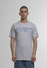Grå bomulds t-shirt med blå ROCAWEAR-logo og etableringsdato. Korte ærmer, rund hals, lige kant og standard pasform.