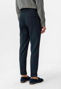 Marineblauwe gestreepte broek met een tapered fit, voorzien van een opgerolde zoom en een achterzak. Gekocht met een lichtgrijze lange mouwen shirt en marineblauwe schoenen.