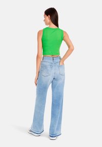 Green cropped tank top with a scalloped hem, paired with light blue wide-leg jeans featuring back pockets and visible stitching.