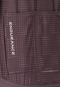 Haut de sport bordeaux avec un motif à pois blancs, comportant le mot "ENDURANCE". Le design inclut des poches et un tissu lisse et texturé.