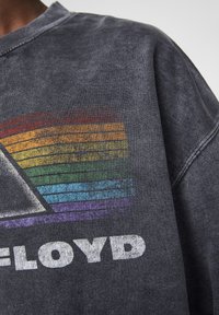 Sudadera negra con un lavado vintage, que presenta un gráfico de triángulo multicolor en tonos de arcoíris y el texto en negrita "FLOYD" en blanco en la parte frontal.