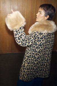 Παλτό με λεοπάρ σχέδιο, με μπεζ ψεύτικη γούνα στον γιακά και τα μανίκια. Μακρυμάνικο, μήκους μέχρι τ η μέση. Λείο ύφασμα, κρέμεται μπροστά σε ξύλινο φόντο.