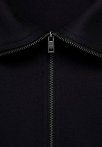 Black zippered collar jacket featuring a metal zipper with a matte finish. Soft texture, simple design, and reinforced stitching along the edges.