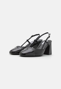 Sorte slingback hælede sko med blank tåhætte og mat læderkrop. Med blokhæle og smal justerbar rem.