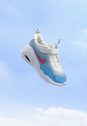 Scarpa sportiva bianca e blu con logo rosso e cinturino bianco che fluttua contro uno sfondo di cielo azzurro limpido.