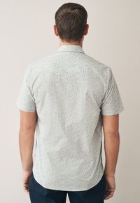 Camicia a maniche corte con sfondo chiaro caratterizzata da un colorato motivo floreale, dettaglio collo e orlo arrotondato. Realizzata in tessuto morbido.