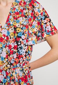 Floral dress featuring a multi-colored pattern of red, yellow, blue, and black on a lightweight fabric; cap sleeves and a v-neck design.