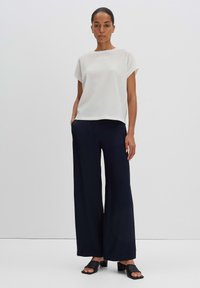 Top corto bianco con texture abbinato a pantaloni navy a gamba larga e scarpe nere senza lacci. Design semplice con una vestibilità rilassata e tessuto morbido.