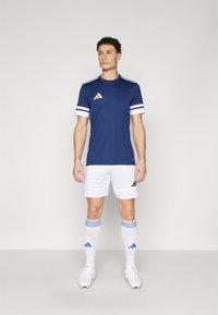 Navy blue athletic shirt with white stripes, paired with white shorts. White soccer socks with blue stripes and black accents on footwear.