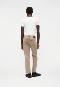 Μπεζ τζιν denim με ίσια γραμμή στο κάτω μέρος, σε συνδυασμό με απλό λευκό μπλουζάκι, εμφανιζόμενα από πίσω. Διαθέτουν δερμάτινο ταμπελάκι στη μέση.