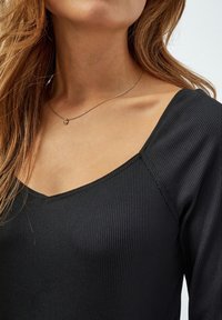 Zwarte geribbelde lange mouw top met een V-hals ontwerp. Heeft een gladde textuur en een aansluitende silhouette. Zilveren ketting met een hart hanger.