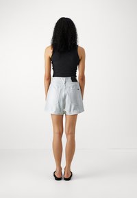 Lyseblå denimshorts med rullet kant, med to baklommer og en liten svart etikett på linningen; parret med en svart tank topp.