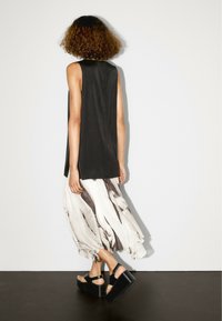 Schwarzes, ärmelloses Oberteil, lockere Passform, kombiniert mit einem fließenden, creme- und schwarzgestreiften Rock. Dicke schwarze Plateau-Sandalen runden das Outfit ab.