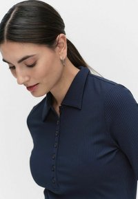 Laivastonsininen ribattuja pitkähihainen polo-paita, jossa on nappisuljenta ja viistot kaulukset. Sileä pinta, istuva malli ja hillitty kiilto.