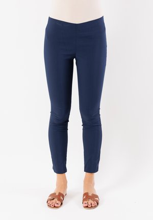 Pantaloni stretch lunghezza caviglia di colore blu navy con un design aderente, caratterizzati da una texture morbida e senza parti metalliche visibili. Indossati con sandali marroni.