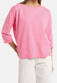 Rosa randig långärmad topp med vid halsringning och trekvartslång ärm. Mjuk tyg med små knappar på vänster axel.