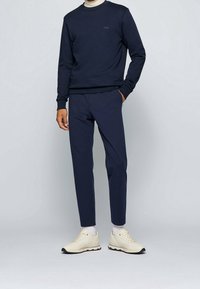 Mörkblå sweatshirt med rund hals och liten logotyp; kombinerad med matchande smal passform mörkblå byxor; beige sneakers; enkel vit bakgrund.