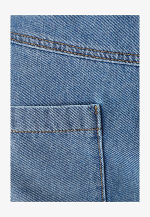 Lichtblauwe denimstof met een zichtbare achterzak, gele stiksels en een gestructureerd weefpatroon. De stof heeft rechte randen en minimale slijtage.