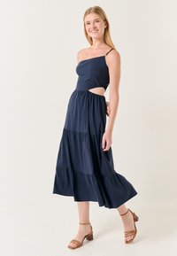 Navyblaues Maxikleid mit einseitigem Design, Cut-Out-Detail an der Taille, gestuftem Rüschesaum und einem glänzenden Akzent am Träger.