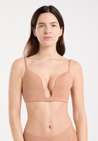 Sujetador de escote pronunciado en tono nude, con tirantes delgados ajustables, diseño sin costuras y textura mate suave, que presenta un escote en forma de V profundo.