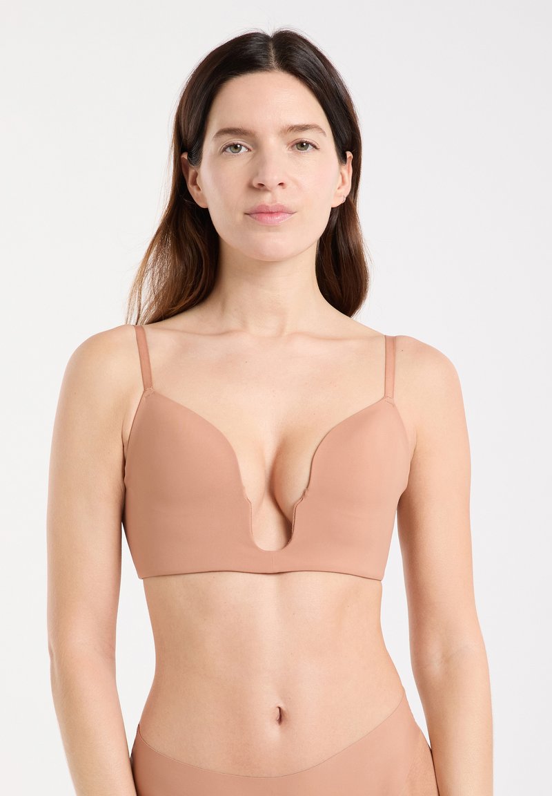 Sujetador de escote pronunciado en tono nude, con tirantes delgados ajustables, diseño sin costuras y textura mate suave, que presenta un escote en forma de V profundo.
