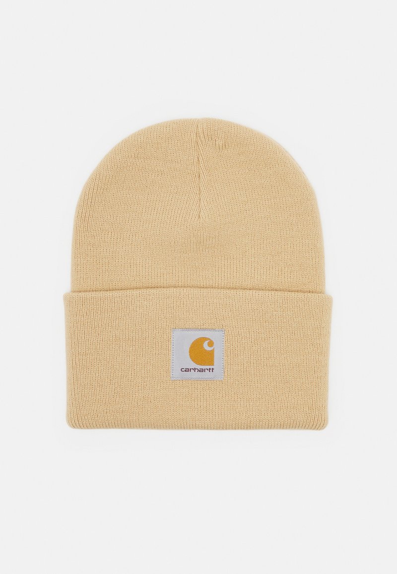 Gelbe gestrickte Beanie-Mütze mit umgeschlagenem Saum und einem quadratischen Logo-Patch, das ein gelbes Icon und Text zeigt. Weiche Textur, leichtes Design.