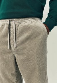 Helle graue Cord-Hose mit vertikaler Rippstruktur, elastischem Taillenbund und Kordelzug. Ausgestattet mit Taschen und entspannter Passform.