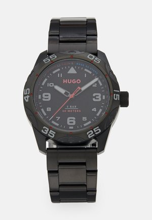 Black stainless steel watch with a round case, analog display, bold numbers, and red accents. Water-resistant up to 50 meters.
