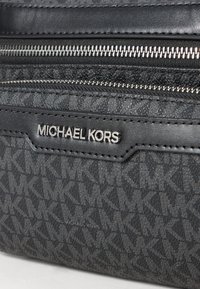 Borsa nera Michael Kors con motivo MK in rilievo, due zip argento e una placca logo in metallo argentato su materiale testurizzato.