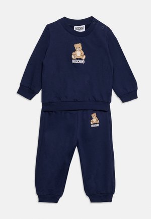 Tmavomodrý detský komplet s dlhými rukávmi a nohavicami, obsahuje medvedíka a logo Moschino na hrudi a nohe.