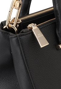 Zwarte leren handtas met een gestructureerde afwerking, gouden hardware, een ritssluiting en een metalen label met de merknaam.