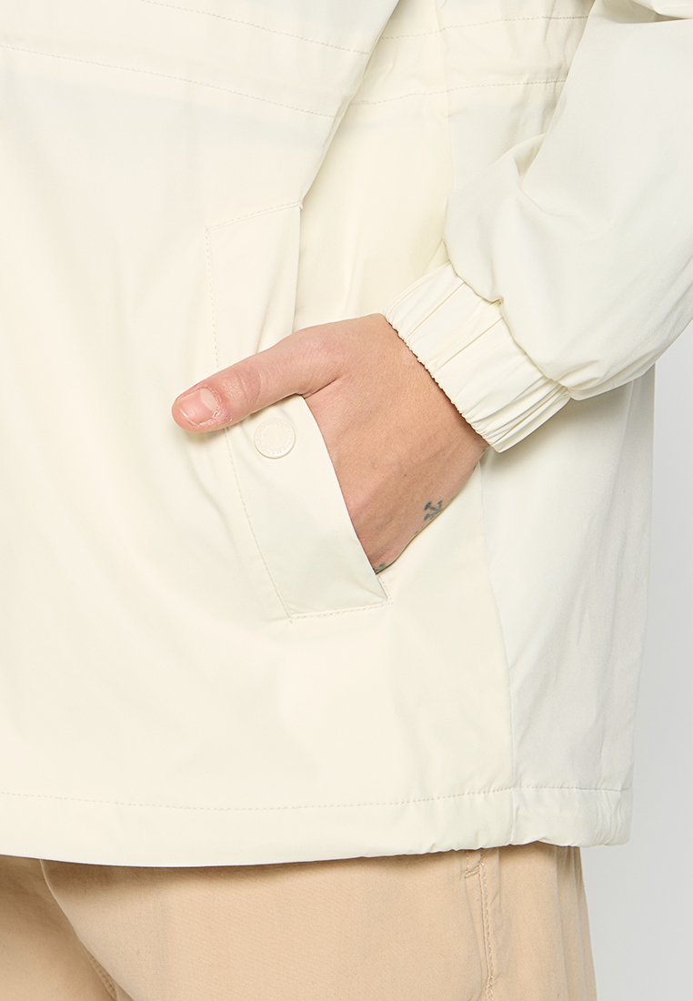 Giacca leggera di colore chiaro realizzata in tessuto morbido. Presenta una tasca laterale, polsini elasticizzati e un design pulito e semplice.