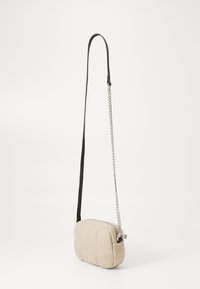 Borsa a tracolla in tessuto beige con design trapuntato, una tracolla nera regolabile e un accento in catena argentata. Presenta una chiusura con zip.
