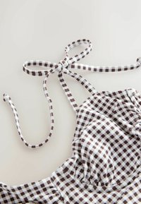 Haut de bikini à carreaux marron et blanc avec bretelles spaghetti nouées sur un fond clair.