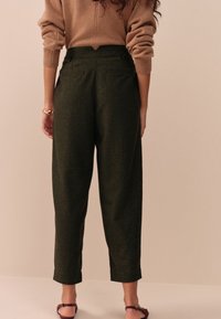 Pantaloni verde închis cu un material texturat, asemănător lânii, talie înaltă și manșete întoarse. Au două buzunare în spate și detalii cu nasturi.