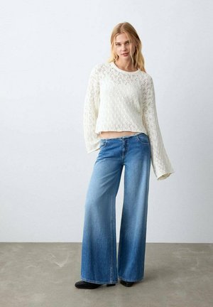 Haut blanc à manches longues en tricot avec un motif texturé, associé à un jean en denim bleu moyen à jambes larges. Style lisse et décontracté.