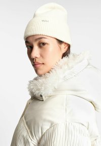 Vit puffjacka med krage i konstpäls, ribbad vit mössa och slät textur. Sidoprofilvy som framhäver egenskaper och material.