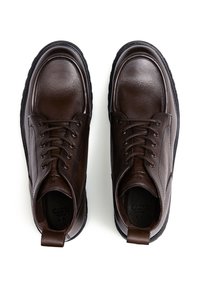 Bruine leren schoenen met een gladde afwerking, ronde neus en zwarte rubberen zolen. Voorzien van veters en een achterste trekstrip voor gemakkelijk aan- en uittrekken.